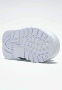Hvit snøresko såle med teksturert gummi, distinkte sirkulære og lineære mønstre, og et Reebok-logo preget på mellomsålen.