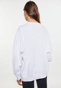 Felpa bianca oversize con spalle scese e polsini a costine. Tessuto morbido con una vestibilità rilassata, dotata di un collo rotondo e senza loghi visibili.