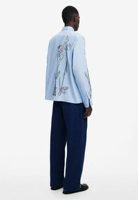Light blue long-sleeve shirt with floral embroidery on the back, paired with dark navy wide-leg pants and black sandals.