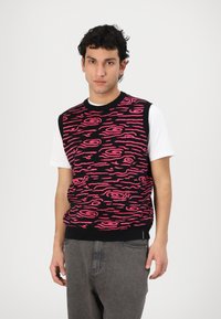 Zwarte mouwloze trui met een roze abstract patroon van spiralen. Draag het over een wit shirt, met een geribbelde halslijn en zoom.