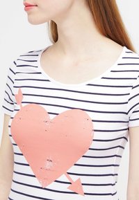 Camiseta de manga corta a rayas en blanco y azul marino, con un gran gráfico desgastado de un corazón rosa y una flecha en la parte frontal.