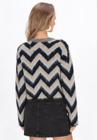 Flauschiger Pullover mit Zickzackmuster in Schwarz, Beige und Hellblau, kombiniert mit einem schwarzen Denim-Minirock mit Gesäßtaschen.