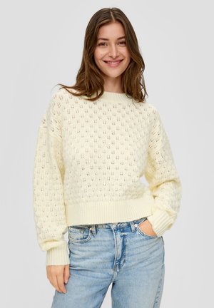 Un pull en tricot jaune clair avec des mailles ajourées en forme de losanges, des poignets et un ourlet côtelés, associé à un jean en denim bleu.