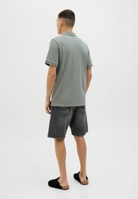Polo grigio, maniche corte, abbinato a pantaloni corti in denim grigio scuro. Scarpe slip-on nere. Design minimalista, texture liscia.