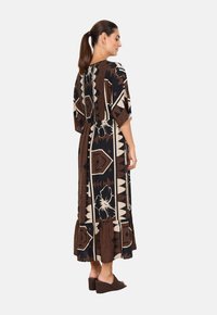 Maxikleid in Schwarz, Braun und Creme mit einem abstrakten geometrischen Muster. Weicher Stoff, lockere Silhouette, kurze Ärmel und ein geraffter Saum.