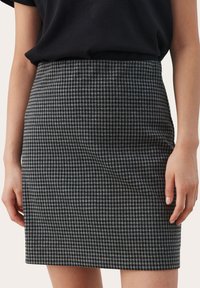 Harmaan ja mustan houndstooth-kuosiset hameet, joissa on vartalonmyötäinen siluetti, sileä pinta ja vyötäröosa. Kankaassa on hienovarainen kiilto ja selkeät kuviot.