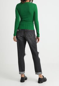 Grünes geripptes Langarmoberteil kombiniert mit hoch taillierten schwarzen Jeans mit ausgefranzten Säumen und schwarzen Schnürschuhen.