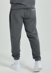 Fleece joggingbroek in donkergrijs met geribde boorden en tailleband, voorzien van een zachte textuur en een relaxte pasvorm. Gecombineerd met witte sneakers.