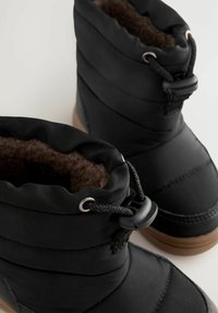 Schwarze isolierte Stiefel mit gepolstertem Stoff, strukturiertem braunem Futter, elastischen Schnürsenkeln und Gummisohlen. Mit einem gerafften Bund am oberen Ende.