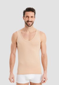 Light beige tank top made of soft fabric, featuring a scoop neckline and wide shoulder straps. Worn with white shorts.