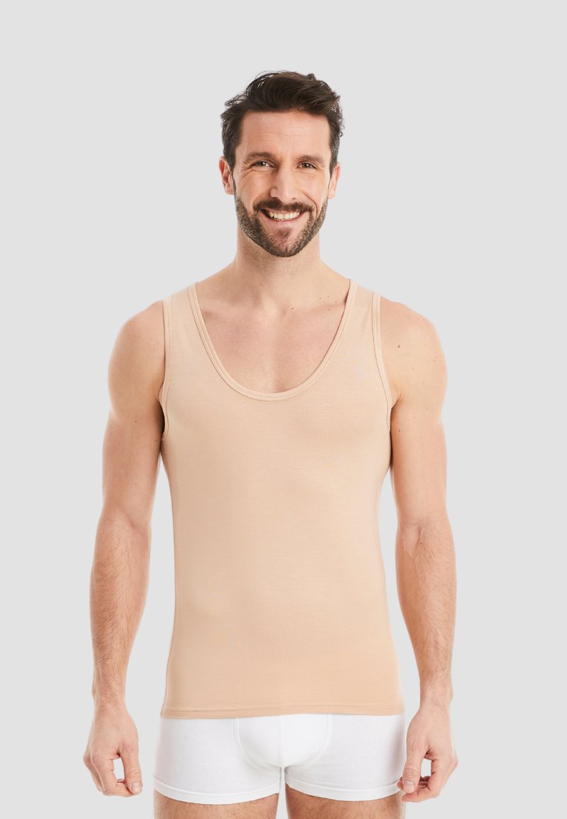 Light beige tank top made of soft fabric, featuring a scoop neckline and wide shoulder straps. Worn with white shorts.