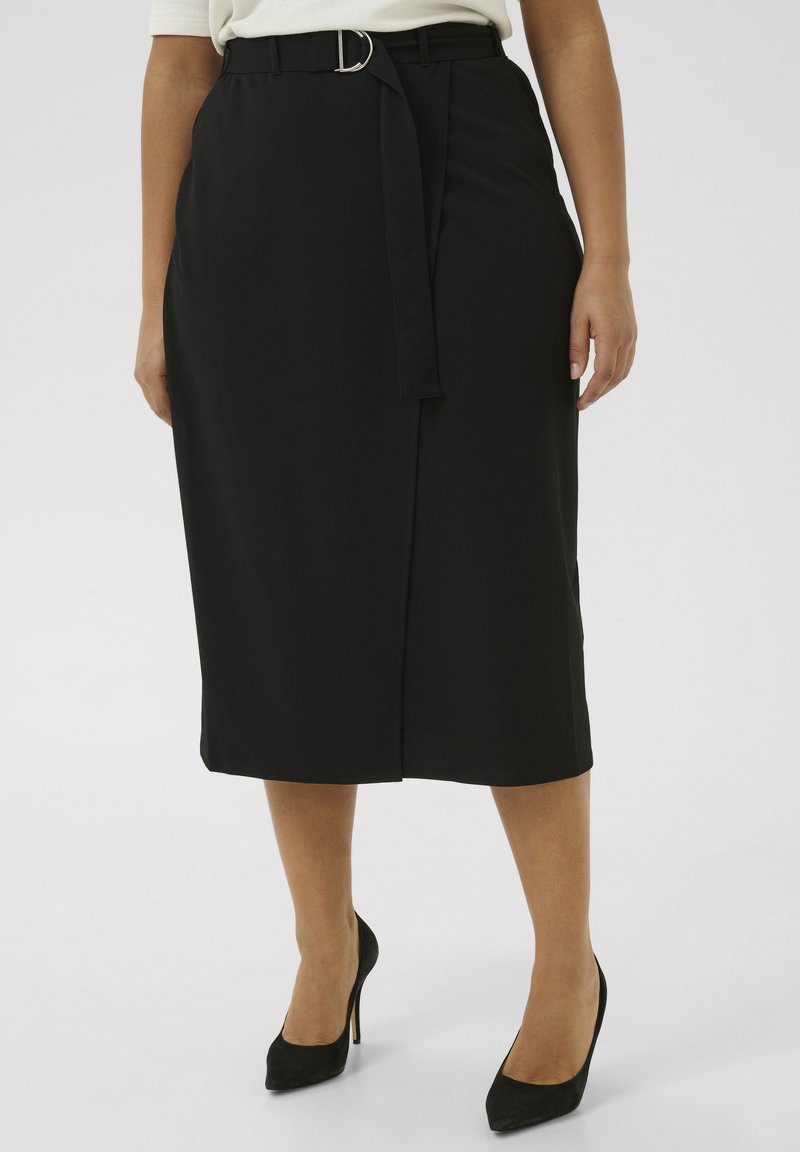 Jupe midi noire avec une ceinture ornée d'une boucle en argent, fabriquée dans un tissu lisse, avec une fente à l'avant et une coupe ajustée, associée à des escarpins noirs.