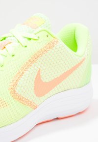 Baskets de sport vert néon avec un dessus en maille respirante, des accents rose clair et une semelle blanche ; présente un emblème Nike en orange bien visible.