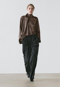 Blouse en satin marron avec un détail noué au col, associée à un pantalon noir plissé taille haute. Texture lisse et coupe décontractée.