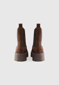 Botas de tobillo de ante marrón con paneles laterales elásticos, acabado texturizado y suelas de goma gris gruesas. Presenta tiradores para facilitar su puesta.