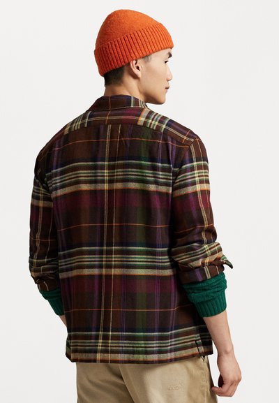 Bruin geruit flanellen shirt met groene gebreide manchetten. Heeft veelkleurige strepen in paars, oranje en wit. Vouwkraag en knoopsluiting aan de voorkant.