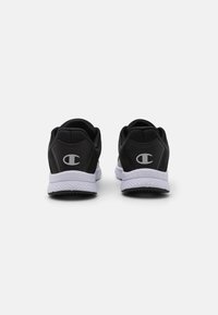 Chaussures de sport noires avec un dessus texturé, un col matelassé et une semelle blanche. Présente un logo au niveau du talon et une semelle extérieure noire crantée.