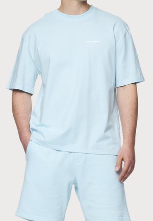 Jasnoniebieska bawełniana koszulka z krótkim rękawem i okrągłym dekoltem, z subtelnym białym napisem "PEGADOR" na piersi. W komplecie z dopasowanymi szortami.