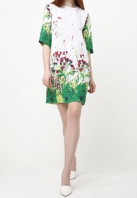 Vestido de manga corta con base blanca, que presenta patrones florales coloridos en verde y rosa. Tela ligera, corte holgado, diseño hasta la rodilla.