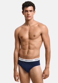 Marineblaue Herrenunterhosen mit einem weißen elastischen Bund, der wiederholt die Markeneinschrift "GANT" trägt. Glatte Stoffqualität mit figurnahem Sitz.