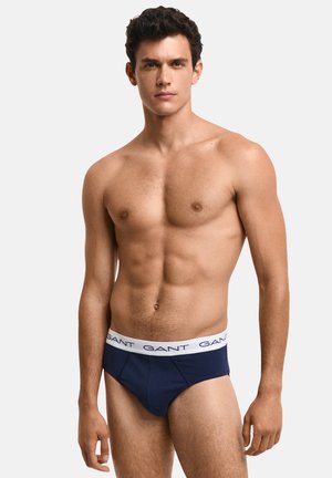 Navy blue men's briefs with a white elastic waistband featuring repeated "GANT" branding. Smooth fabric with a snug fit.
