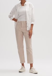 Ljust beige bomullbyxor med rak passform, tillsammans med en vit linne och en skjorta med knappar. Modell som bär vita sneakers.