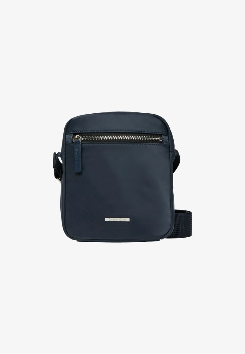 Borsa a tracolla blu navy in materiale resistente, con tasca frontale con zip, tracolla regolabile e una piccola placca con logo sul davanti.