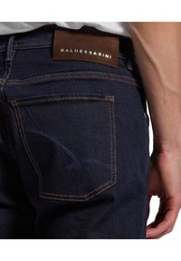 Dunkelblaue Jeans aus Denim mit kontrastierendem orangem Stich. Verfügt über ein Lederpatch mit dem „BALDESSARINI“-Label am Bund und Details an der Gesäßtasche.