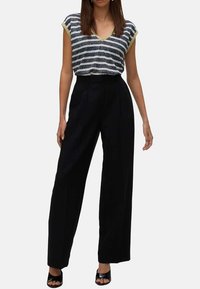 Haut à rayures bleu marine et blanc en v avec des finitions jaunes, associé à un pantalon large noir taille haute et des sandales à talons noires.