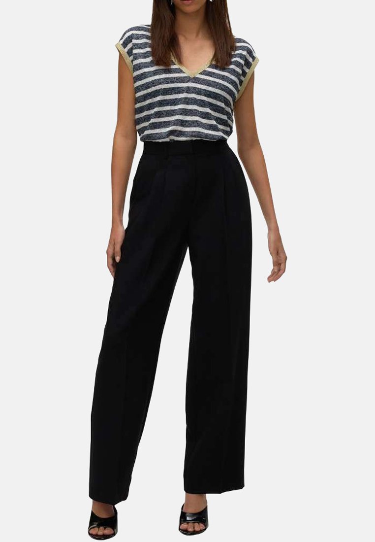 Haut à rayures bleu marine et blanc en v avec des finitions jaunes, associé à un pantalon large noir taille haute et des sandales à talons noires.