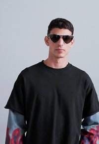 Cămașă neagră cu mânecă scurtă și finisaj texturat. Design supradimensionat cu mâneci în model de flăcări, albastre și roșii. Ochelari de soare întunecați cu o formă unică.