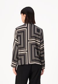 Long-sleeve shirt in black and cream featuring a geometric line pattern. Soft fabric, relaxed fit, and a straight hem at the back.