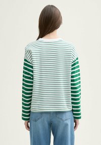 Camisa de manga larga a rayas verdes y blancas con cuello redondo; corte relajado; tejido ligero; vista trasera que muestra una costura simple y un dobladillo redondeado.