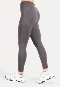Leggings gris taille haute, design ajusté. Caractéristiques : panneaux texturés et tissu lisse. Portés avec des chaussures de sport blanches.