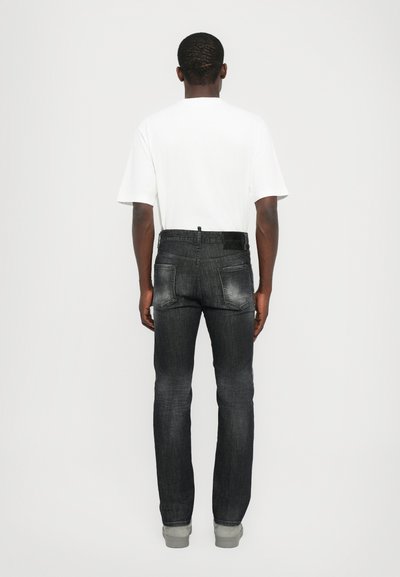 Jeans de denim negro con un ajuste slim, con una textura desgastada, cinco bolsillos y una cinturilla trasera con trabillas para el cinturón. Llevados con una camiseta blanca.