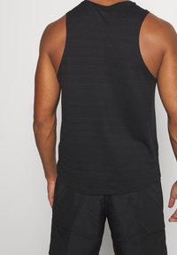 Top sin mangas negro con un patrón texturizado, escote redondeado y dobladillo ligeramente curvado, combinado con pantalones cortos negros.