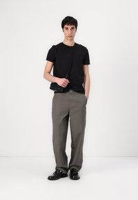Zwart t-shirt, losse grijze broek, zwarte schoenen en een kleine schoudertas. Gladde textuur, eenvoudig ontwerp, casual uitstraling.