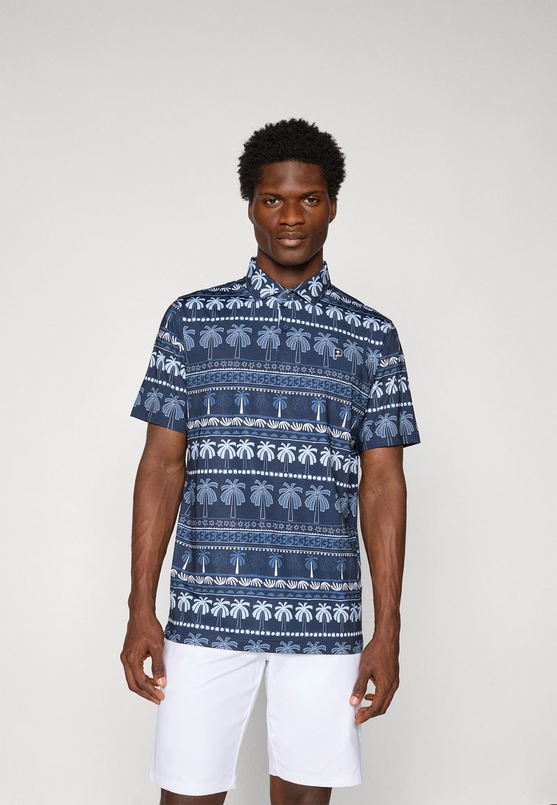Marineblå kortærmet polo shirt med palmeprint, knapkrave og afslappet pasform, parret med hvide shorts.