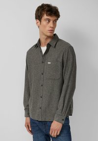 Grijze flanellen shirt met een button-down kraag, een borstzak en een subtiele textuur, gecombineerd met blauwe jeans en donkere knopen.