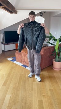 Juodas odinis bomber tipo švarkas su užtrauktuku, džinsiniu audiniu ant rankovių ir didelėmis paminkštintomis rankovėmis. Rodomas ant asmens vidinėje aplinkoje.