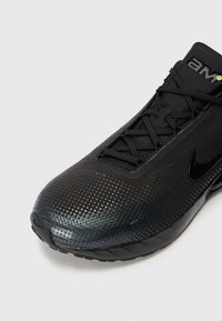 Black athletic shoe with perforated upper, rounded toe, lacing system, and matte finish. Features a visible Nike logo and textured sole.