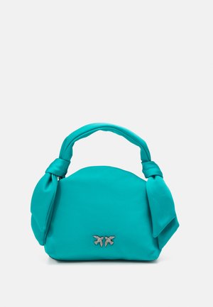 Bolso turquesa con forma redondeada y asas anudadas. Presenta un acabado texturizado y un emblema decorativo plateado en la parte frontal.