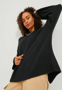 Črni oversized pulover z teksturirano tkanino, rebrastimi manšetami in robom, sproščen silhuet in razporkoma na straneh.