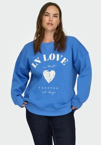 Sudadera azul de tejido suave, con un corte holgado, puños de canalé y texto impreso en blanco con un diseño de corazón en la parte delantera.