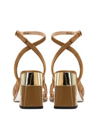 Sandali con tacco in suede marrone, dotati di cinturini incrociati, dettagli metallici sul tacco e una base spessa e lucida per stabilità e supporto.