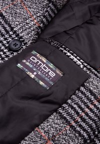 Grå houndstooth frakke med røde accenter, med en sort inderforing og et mærke mærket "OMBRE QUINTESSENCE M" med en struktureret overflade.