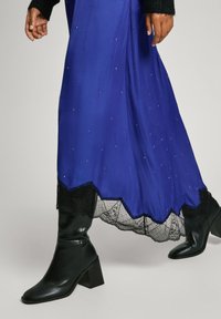 Długa, zwiewna sukienka w kolorze królewskiego niebieskiego z rozsypanymi ozdobami i czarną koronkową podszewką. W połączeniu z eleganckimi czarnymi botkami na obcasie.