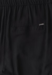 Shorts en tissu noir avec taille élastique, poche latérale et petite étiquette en métal. Texture lisse et design minimaliste.
