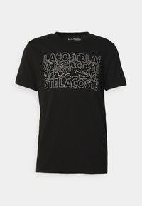 Černé bavlněné tričko s velkým bílým nápisem "LACOSTE" a grafikou krokodýla. Krátké rukávy a kulatý výstřih. Měkká textura.