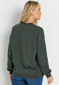 Felpa verde dal fit morbido, con collo e polsini a coste, realizzata in cotone soffice, abbinata a jeans blu.